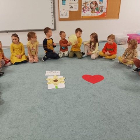 Powiększ obraz: Dzieci siedzą w kole i przekazują sobie żółty balonik – symbol życzliwości