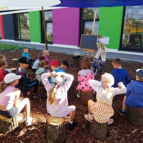 Powiększ obraz: Przedszkolaki słuchają fragmentu książki czytanej w sali zewnętrznej w ogrodzie sensorycznym