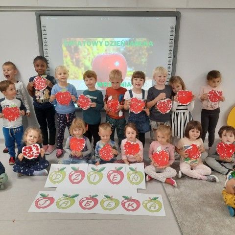 Powiększ obraz: Dzieci trzymają prace plastyczne i napis dzień jabłka