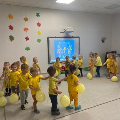 Powiększ obraz: Dzieci tańczą w kółeczku. Każde z nich trzyma żółty balon – symbol Dnia Życzliwości i Pozdrowień