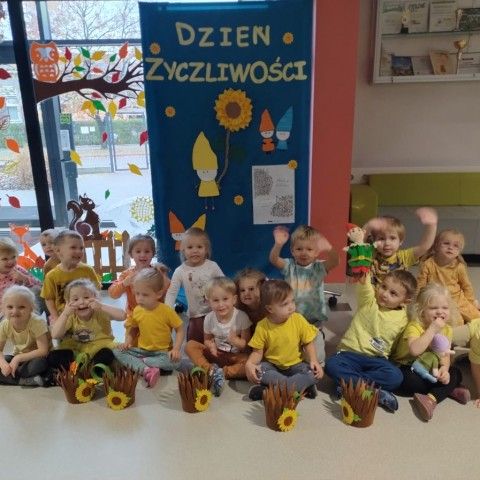 Powiększ obraz: Przedszkolaki pozują do zdjęcia, siedząc przed dekoracją wykonaną z okazji Dnia Życzliwości
