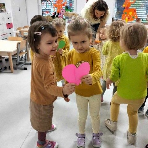 Powiększ obraz: Dzieci ubrane na żółto, tańczą w parach trzymając papierowe serduszko – symbol życzliwości