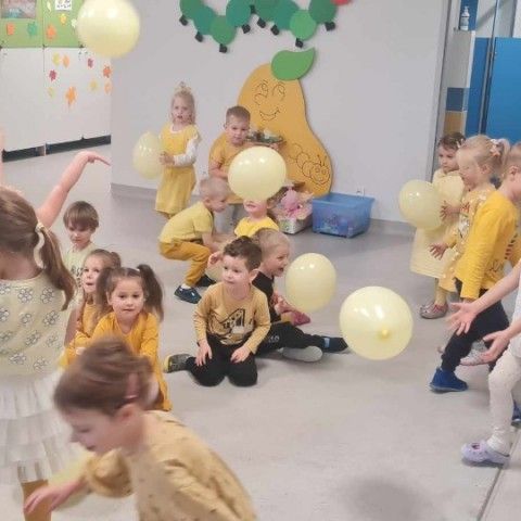 Powiększ obraz: Przedszkolaki bawią się na dywanie żółtymi balonami, które symbolizują życzliwość