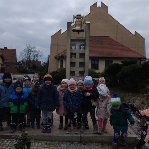 Powiększ obraz: Zdjęcie przedszkolaków na tle dzwonu na wieży kościoła parafialnego
