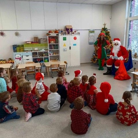 Powiększ obraz: Dzieci siedzą na dywanie i rozwiązują zagadki, które zadaje im Mikołaj