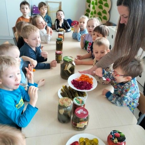 Powiększ obraz: Dzieci siedzą i zajadają różne przetwory warzywne