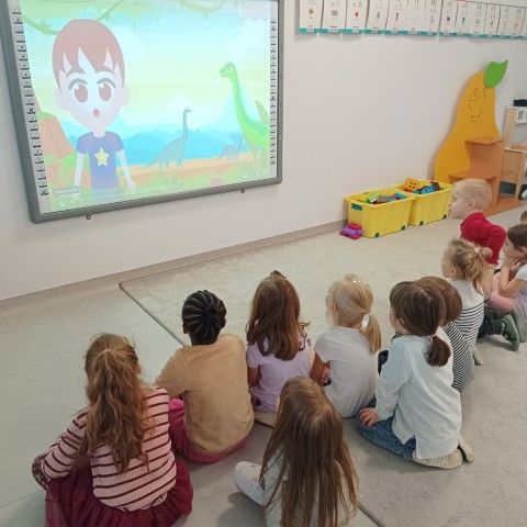 Powiększ obraz: Dzieci oglądają film edukacyjny o dinozaurach