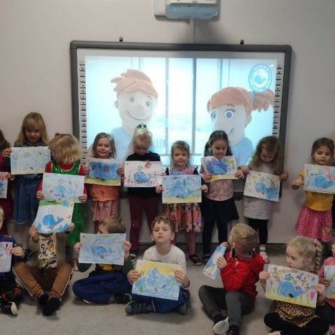 Powiększ obraz: Dzieci prezentują prace plastyczną z logiem Akademii Przyjaciół Wody
